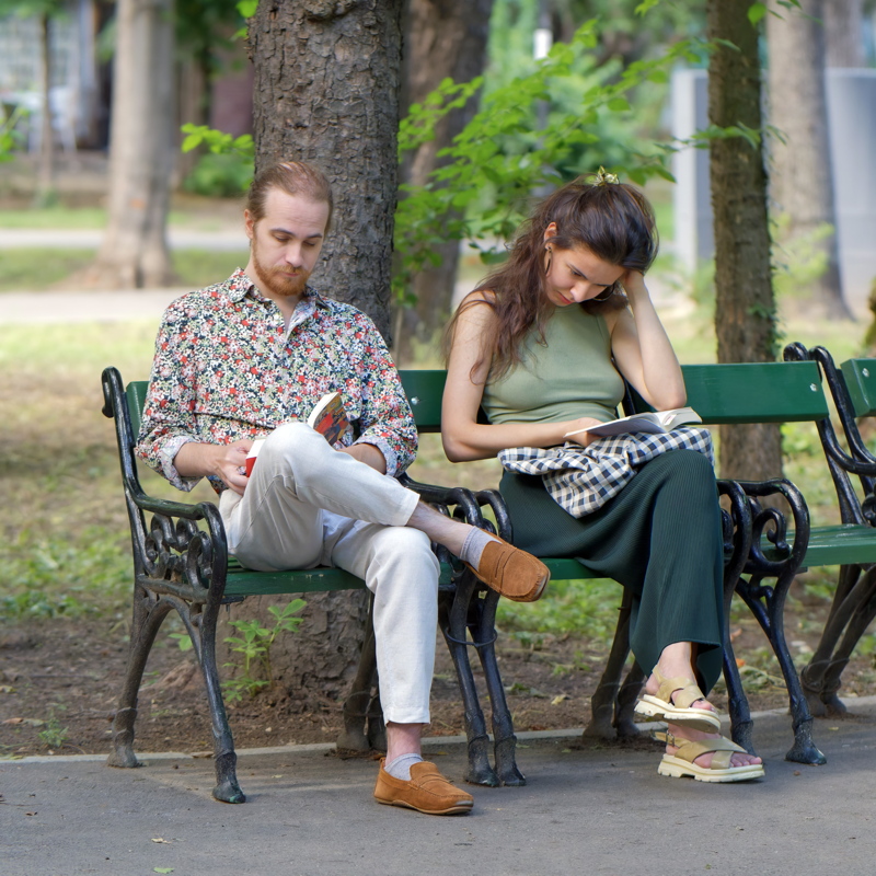 14 - Two individuals reading books while relaxing on a park bench